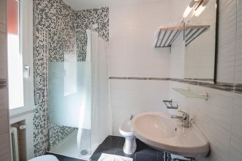 A modern bathroom with mosaic-tiled walls, a glass shower enclosure, and sleek fixtures offers a clean and stylish space ideal for travelers seeking comfort and functionality.