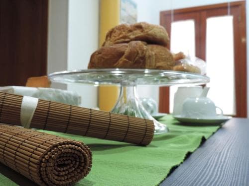 A cozy breakfast nook features a green tablecloth, bamboo placemats, a glass cake stand with croissants, and white teacups, evoking a serene morning ambiance ideal for a relaxing getaway.