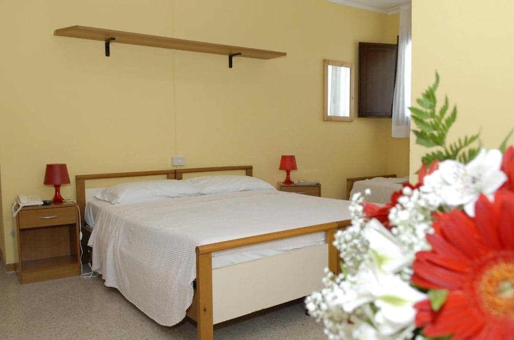 A cozy hotel room with yellow walls, wooden furniture, red lamps, and fresh flowers creates a warm and inviting atmosphere ideal for travelers seeking comfort and relaxation.