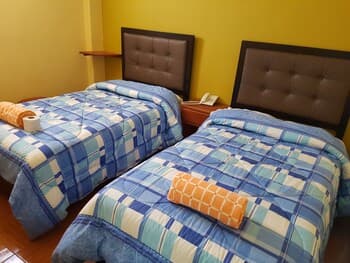 A cozy hotel room with two neatly made beds featuring blue plaid bedding, a warm yellow wall, and simple furnishings, ideal for budget travelers seeking comfort.