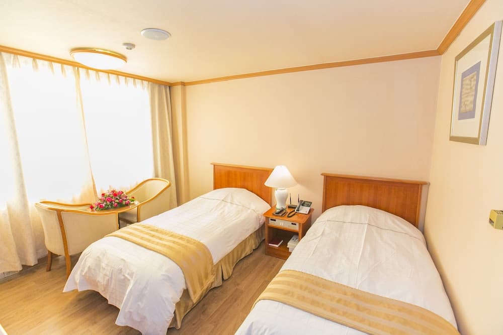 A cozy hotel room with two neatly made beds, warm lighting, a wooden nightstand, and a chair by the window, ideal for travelers seeking comfort and relaxation.
