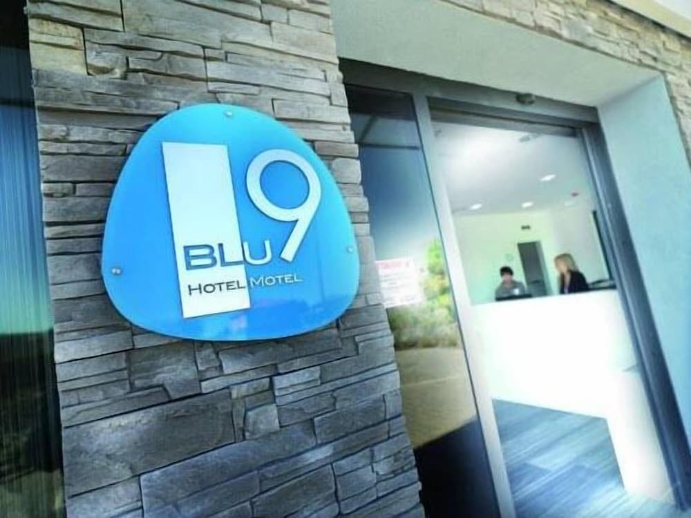 A modern hotel entrance featuring a striking blue "BLU9 Hotel Motel" sign on a textured stone wall invites travelers seeking comfortable accommodations.
