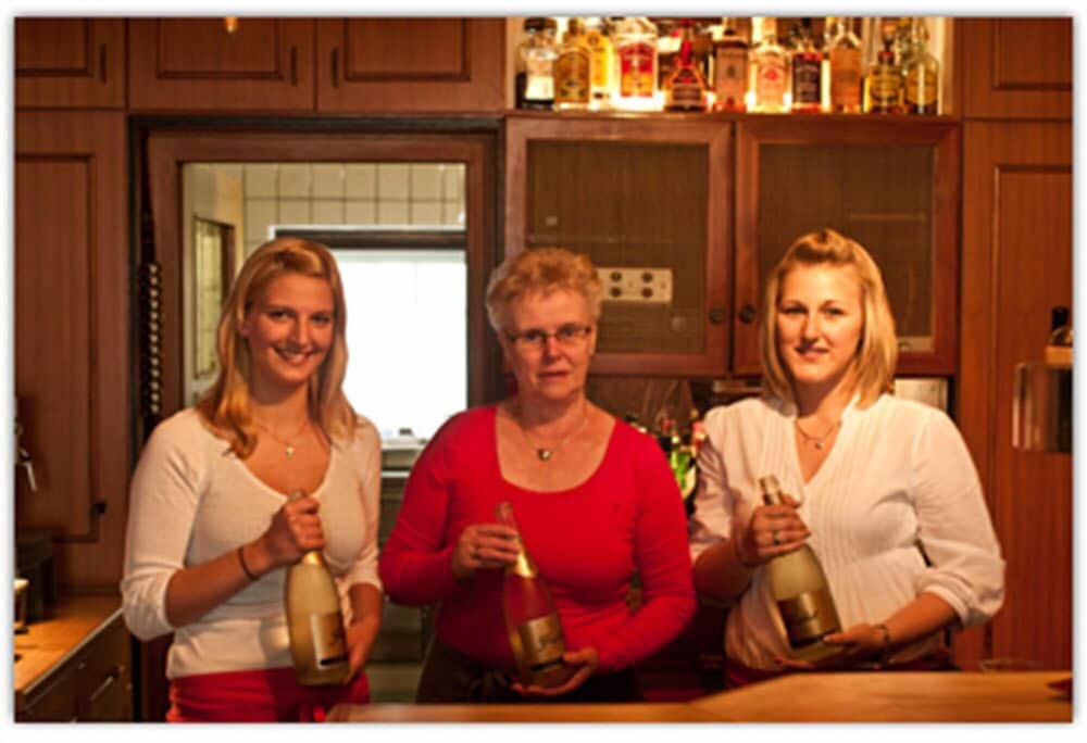 Three women share a cheerful moment in a cozy kitchen, holding champagne bottles, ideal for a family gathering or festive celebration photo.