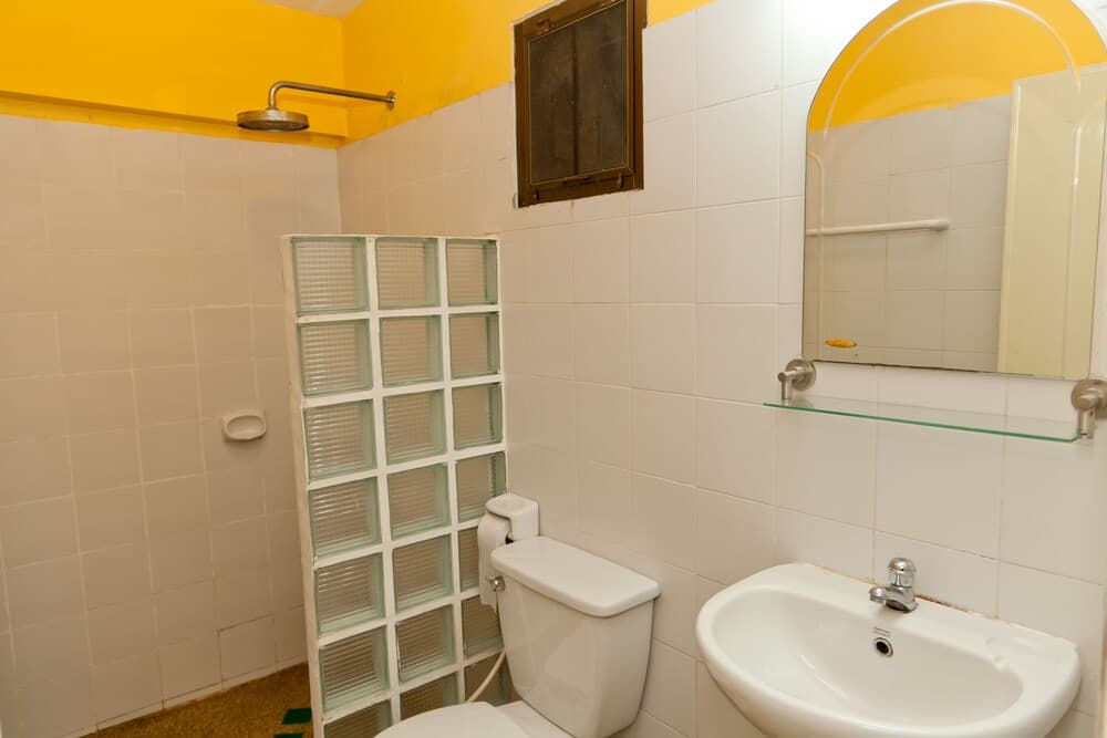 A compact bathroom with white tiled walls, a yellow ceiling, glass block shower partition, and modern fixtures offers a bright and functional space ideal for travelers seeking efficient accommodations.