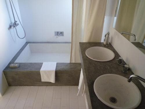 A modern bathroom featuring a minimalist concrete bathtub, dual sinks, and a shower area, ideal for travelers seeking a clean and functional accommodation space.
