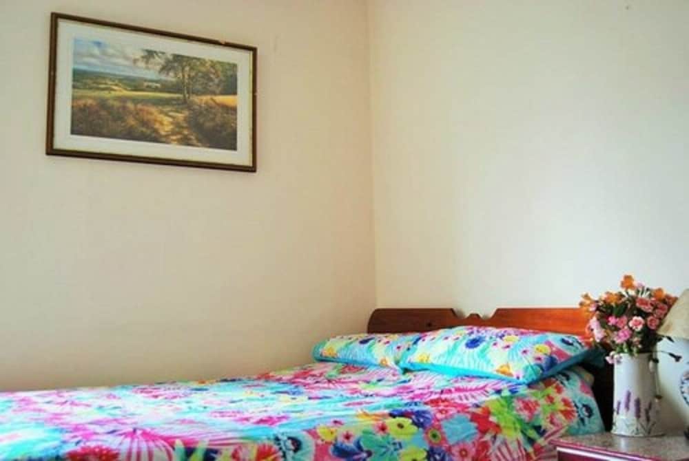 A cozy bedroom with a vibrant floral bedspread, framed landscape artwork, and a vase of fresh flowers creates a welcoming atmosphere ideal for travelers seeking a comfortable and affordable accommodation.