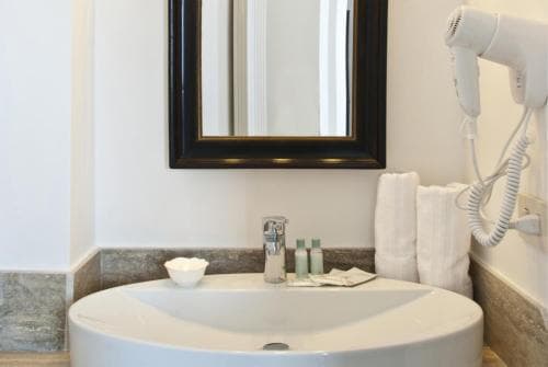 A cozy hotel bathroom features a sleek white sink, a framed mirror, neatly folded towels, and a mounted hairdryer, ideal for travelers seeking comfort and convenience.