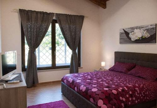 A cozy bedroom with a neatly made bed adorned in purple polka-dot bedding, a desk with a laptop by the window, and soft lighting creates an inviting atmosphere ideal for travelers seeking relaxation and comfort.