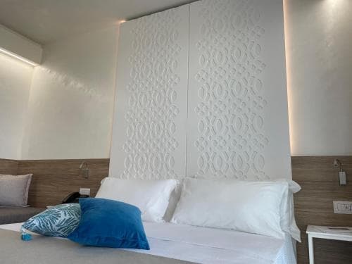 A cozy hotel room features a neatly made bed with white linens and blue pillows against a textured wall, creating a serene and inviting atmosphere ideal for travelers seeking relaxation.