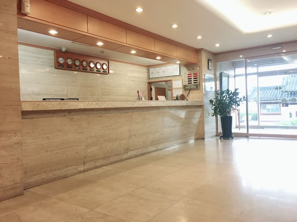A serene hotel lobby features a marble reception desk adorned with clocks, a potted plant, and bright natural light streaming through glass doors, ideal for travelers seeking a calm check-in experience.