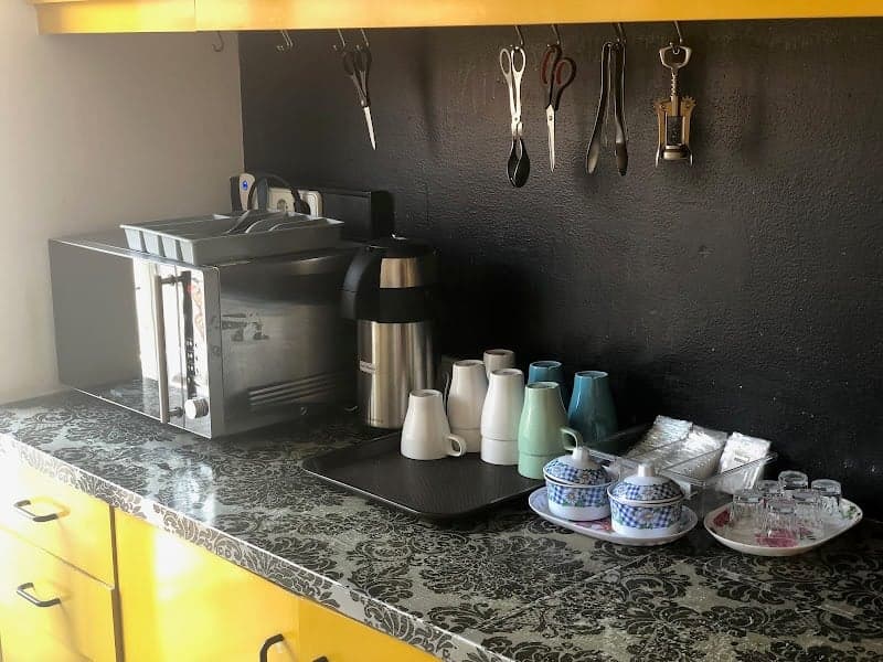 A cozy hostel kitchenette in Lisbon features a microwave, colorful mugs, and hanging utensils on a dark wall, ideal for travelers seeking a self-catering experience.