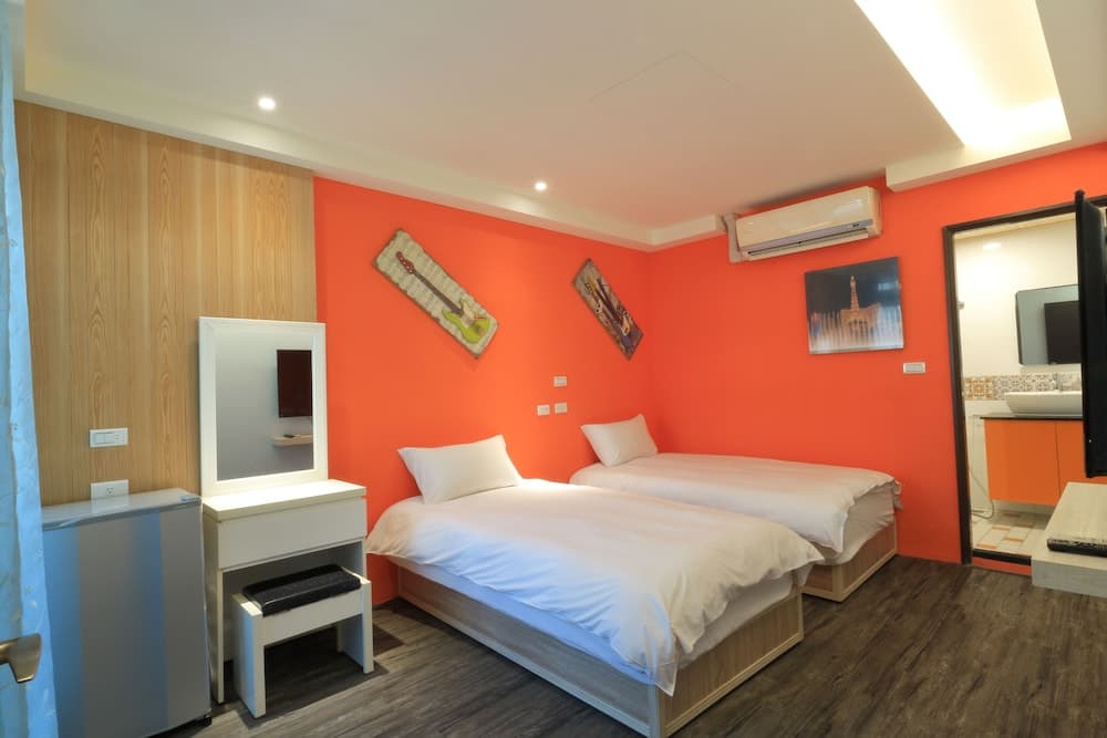 A cozy hotel room with vibrant orange walls, twin beds, guitar-themed decor, and a modern bathroom, ideal for travelers seeking comfort and style.