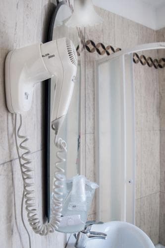 A cozy hotel bathroom features a mounted hairdryer beside a sleek sink and shower area, ideal for travelers seeking convenience and comfort during their stay.