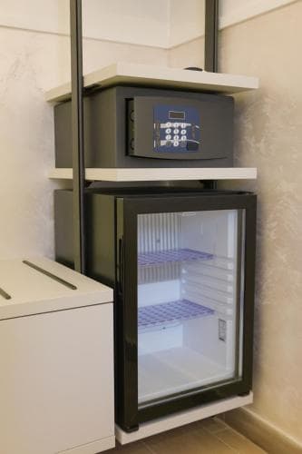 A sleek hotel room corner features a modern mini-fridge and digital safe atop white shelves, exuding a clean and secure ambiance ideal for travelers seeking convenience and safety during their stay.