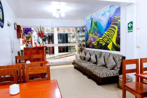 A cozy hotel lobby adorned with vibrant Machu Picchu artwork exudes warmth, featuring wooden furniture, a striped sofa, and floral arrangements, ideal for travelers seeking comfort and cultural ambiance.