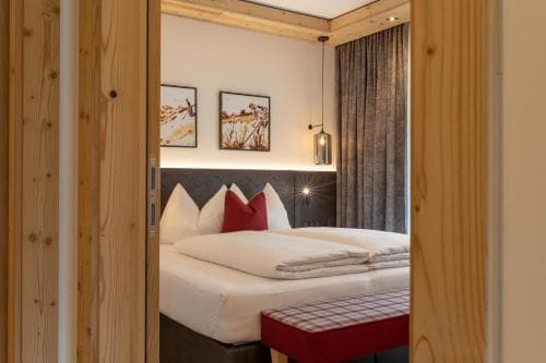 A cozy hotel room with wooden accents, a neatly made bed adorned with red and white pillows, framed artwork on the wall, and warm lighting creates an inviting atmosphere perfect for travelers seeking comfort and relaxation.