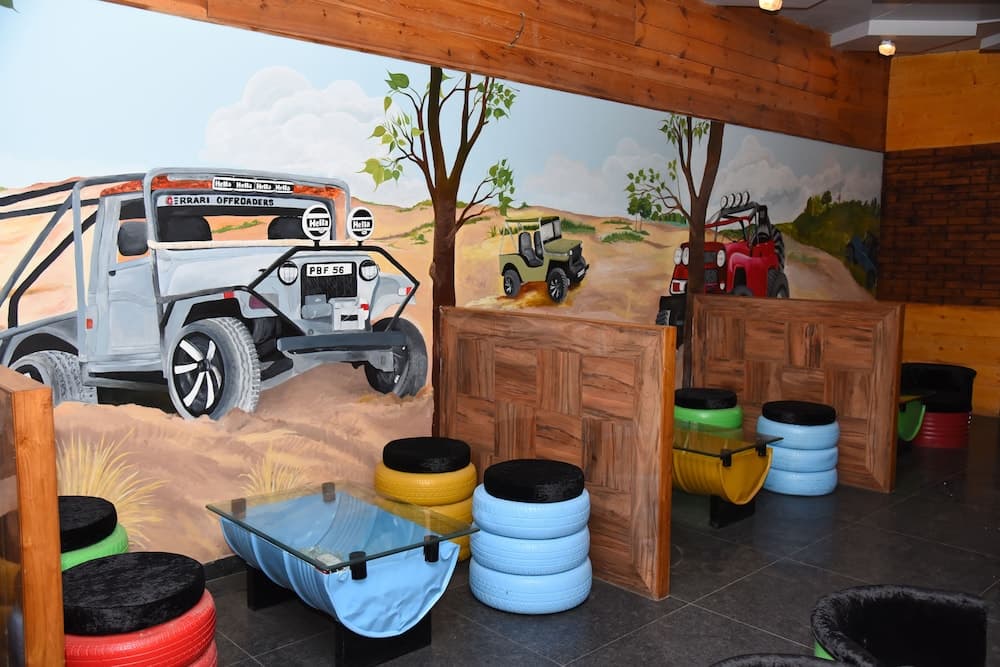 A vibrant indoor play area features a mural of off-road vehicles in a desert landscape, colorful tire seats, and wooden decor, creating an adventurous atmosphere ideal for family-friendly entertainment.