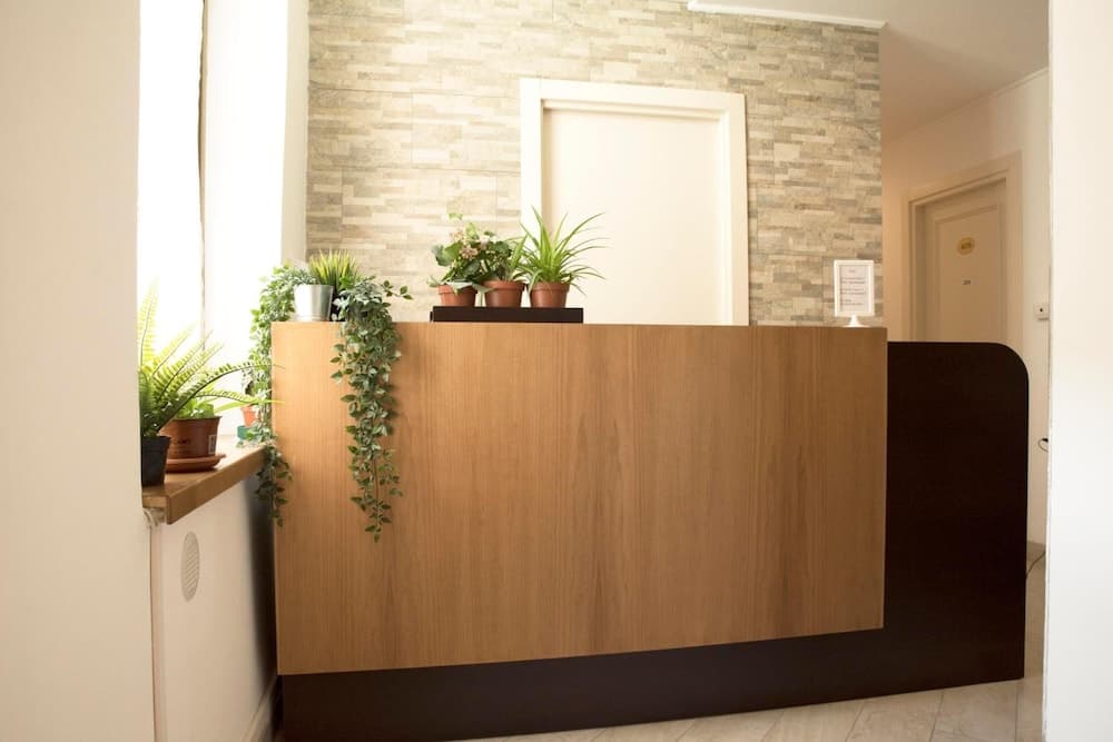 A serene hotel lobby features a modern wooden reception desk adorned with lush green plants, set against a textured stone wall, ideal for travelers seeking a calm and welcoming atmosphere.