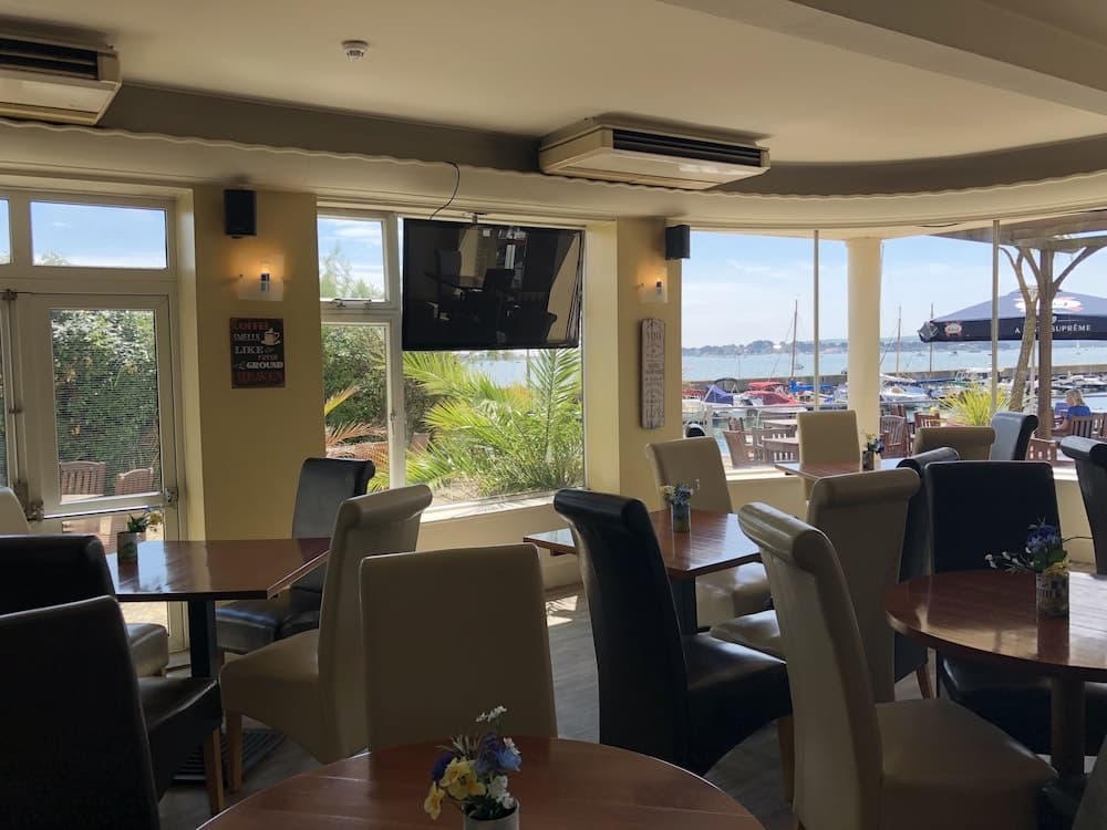 A cozy waterfront café with wooden tables, comfortable chairs, and large windows offering serene views of the marina, perfect for travelers seeking a relaxing dining experience by the sea.