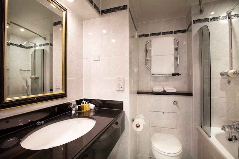 A modern hotel bathroom with sleek marble tiles, a black countertop sink, and a walk-in shower offers a clean and luxurious ambiance ideal for travelers seeking comfort in London accommodations.