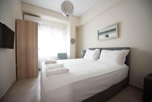 A cozy hotel room features a neatly made bed with white linens, a modern lampshade, and a wall-mounted TV, creating a serene atmosphere ideal for travelers seeking comfort and relaxation.