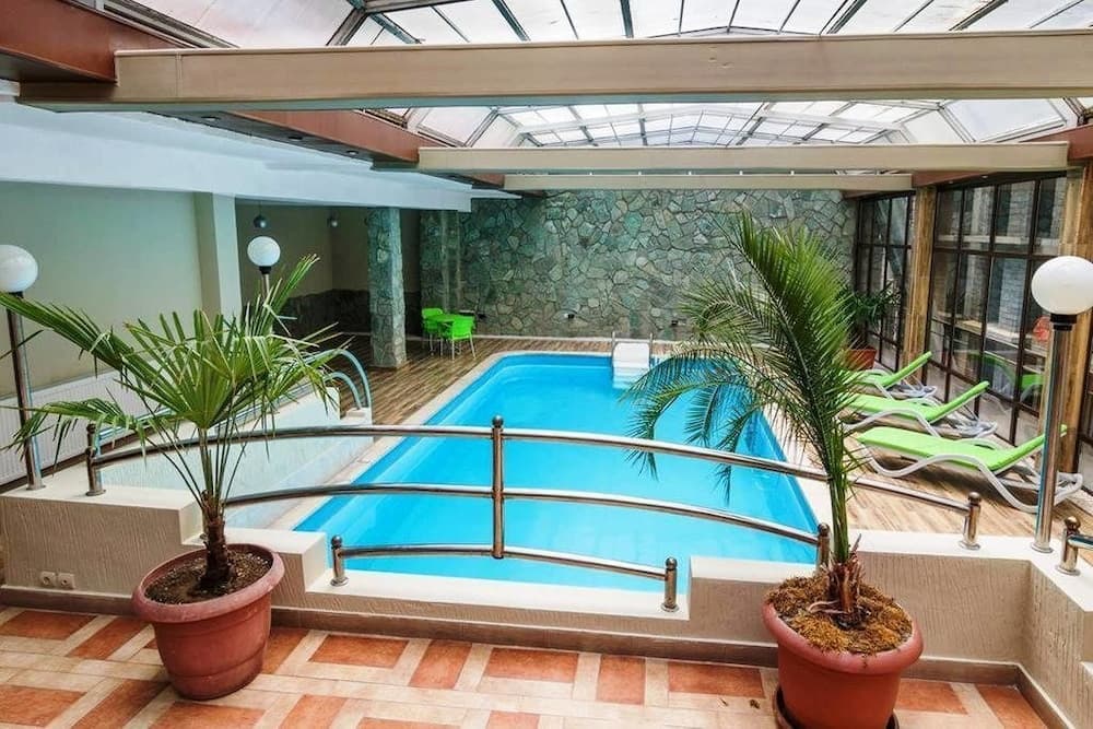 A serene indoor pool area with vibrant blue water, surrounded by lush potted plants, lounge chairs, and a stone wall backdrop, offers a relaxing retreat ideal for travelers seeking rejuvenation in a spa-like setting.