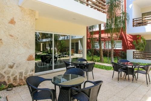 A cozy outdoor patio with modern tables and chairs set against a vibrant backdrop of lush greenery and colorful architecture, ideal for travelers seeking a relaxing dining or lounging spot in a tropical resort setting.