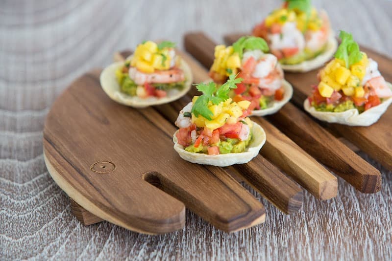 A vibrant display of fresh ceviche tacos garnished with cilantro sits invitingly on wooden paddles, perfect for a relaxing culinary experience at the serene Tembo Beach Club & Resort in Thailand.
