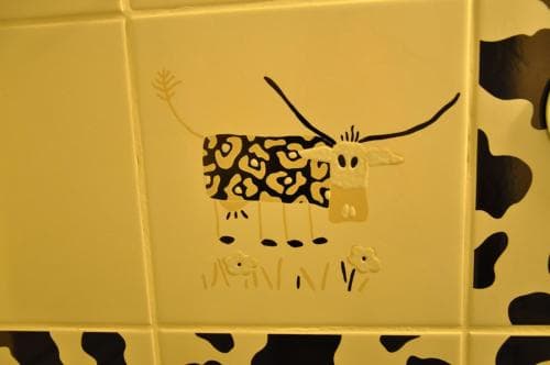A whimsical yellow wall adorned with playful cow art creates a cheerful atmosphere in a children's play area, perfect for family-friendly travel destinations seeking unique decor elements.