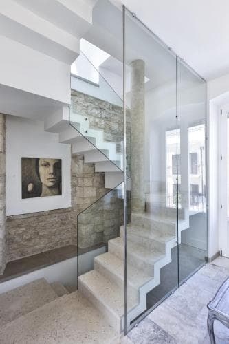 A modern staircase with glass railings ascends through a chic, minimalist interior featuring stone walls, creating an elegant ambiance ideal for luxury home tours or architectural photography.