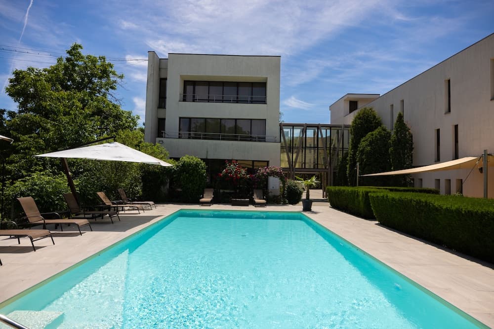 A serene modern villa with a pristine pool, surrounded by lush greenery and lounge chairs under umbrellas, offers an ideal retreat for luxury relaxation.