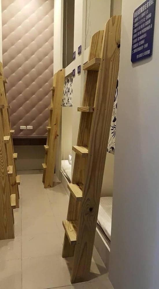A cozy hostel room features wooden bunk beds with ladders, soft pink padded walls, and a calm atmosphere, ideal for budget travelers seeking comfortable accommodations.