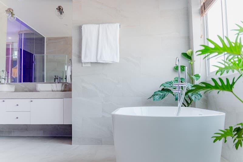 A serene bathroom at LOVE Beach Club Koh Samui features a modern white bathtub, lush green plants, and a sleek vanity, creating a tranquil oasis ideal for travelers seeking relaxation and luxury.