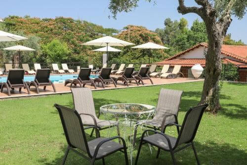 A serene resort scene features lounge chairs under umbrellas by a sparkling pool, surrounded by lush greenery, ideal for relaxing vacations.