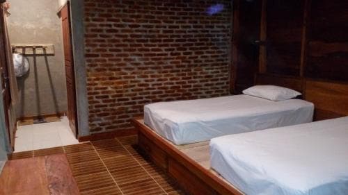 A cozy hostel room with two neatly made beds against an exposed brick wall, featuring wooden flooring and a rustic ambiance, ideal for budget travelers seeking a simple yet charming accommodation.