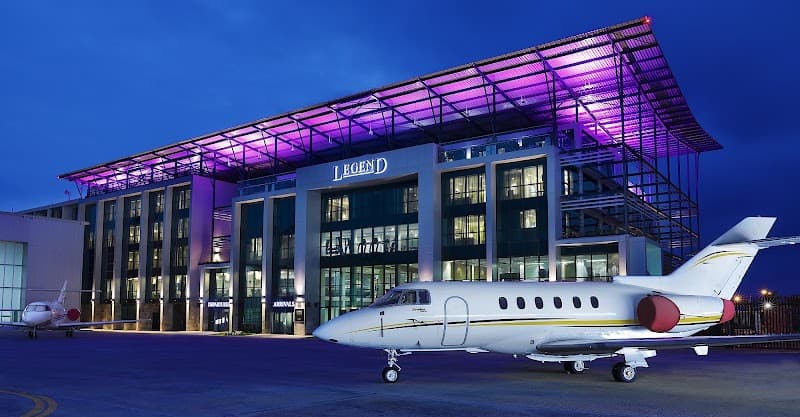 The modern Legend Hotel Lagos Airport, illuminated with vibrant purple lighting, stands prominently near private jets on the tarmac, offering travelers a luxurious stay in a bustling aviation hub.