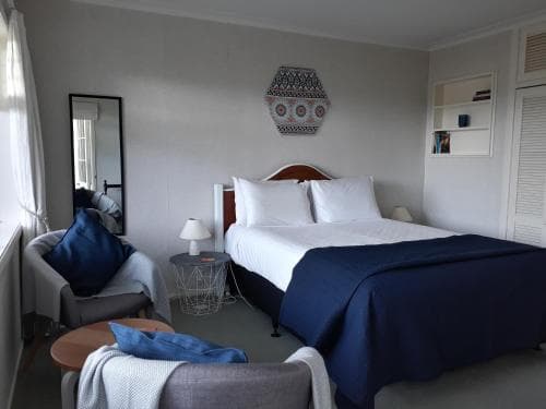 A cozy hotel room features a neatly made bed with navy blue bedding, modern furnishings, and soft natural light filtering through sheer curtains, ideal for travelers seeking comfort and relaxation.