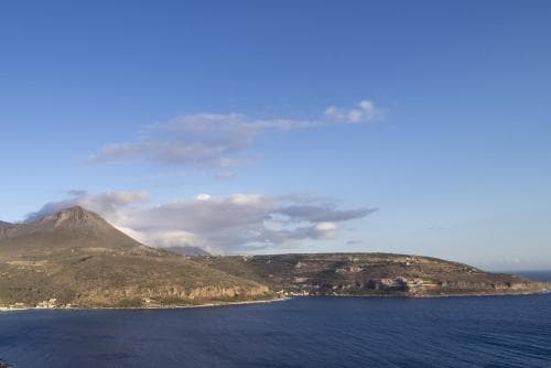 A serene coastal landscape features lush hillsides meeting the calm sea under a partly cloudy sky, ideal for tranquil seaside retreats and scenic cruises.