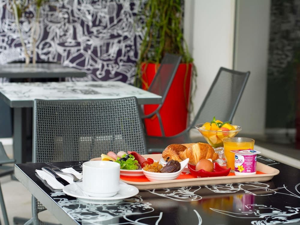 A vibrant outdoor café scene features a colorful breakfast tray with croissants, fruit, and yogurt on a stylish black table, set against an artistic wall mural, perfect for travelers seeking a cozy morning spot.