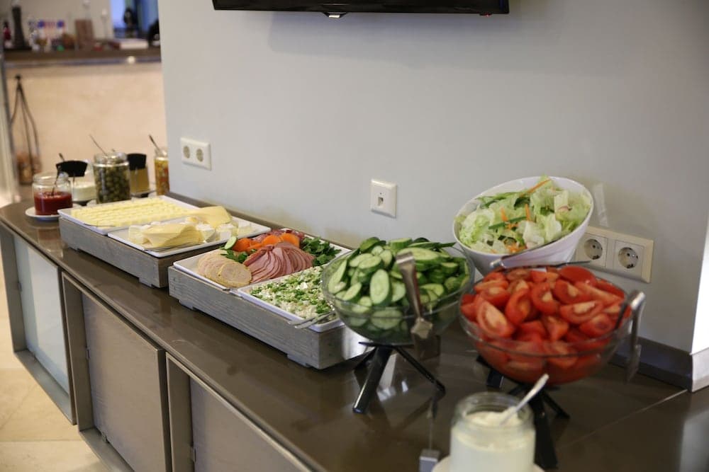 A cozy hotel buffet area features a variety of fresh salads, meats, and cheeses on a sleek countertop, inviting travelers to enjoy a healthy meal in a modern setting.