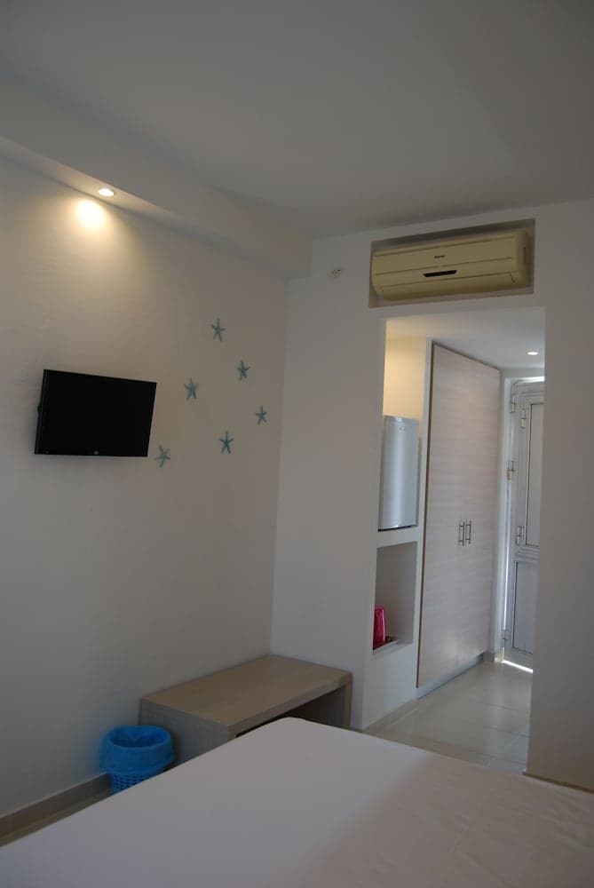 A cozy hotel room with a neatly made bed, wall-mounted TV, starfish decorations, and built-in storage exudes a serene and functional atmosphere ideal for travelers seeking comfort and simplicity.