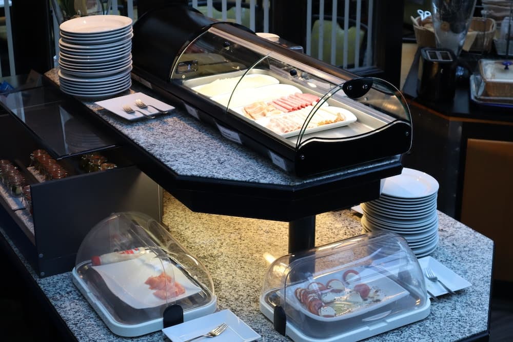 A cozy hotel buffet station features neatly arranged breakfast items under glass covers on a granite countertop, inviting travelers to enjoy a fresh start to their day.