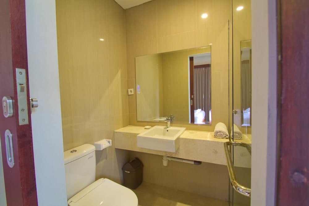 A cozy hotel bathroom features warm beige walls, a sleek sink with a large mirror, neatly folded towels, and a glass shower door, ideal for travelers seeking comfort and cleanliness.