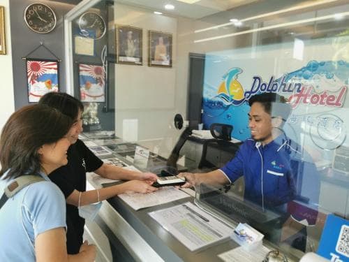 Guests engage in a friendly check-in at a vibrant hotel reception adorned with clocks and artwork, creating a welcoming atmosphere ideal for travelers seeking efficient service.