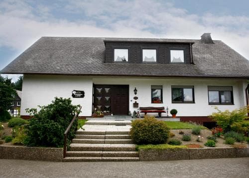 A charming white house with a slate roof and well-maintained garden offers a serene rural retreat, ideal for travelers seeking a peaceful countryside escape.