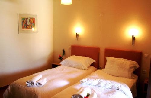 A cozy hotel room features two neatly made beds under warm wall sconces, adorned with a vibrant painting and fresh flowers, ideal for travelers seeking comfort and relaxation.