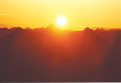 A breathtaking sunset casts a warm glow over a mountainous landscape, creating a serene and majestic scene ideal for adventure seekers and nature photographers.