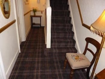 A cozy hotel hallway with plaid carpeting, warm lighting, and a cushioned chair creates an inviting atmosphere perfect for travelers seeking comfort and charm.
