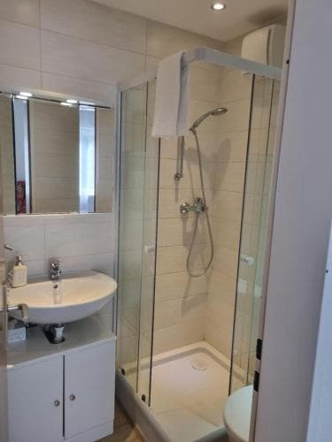 A clean and modern bathroom featuring a glass-enclosed shower, white vanity with sink, and illuminated mirror, ideal for travelers seeking comfort and functionality in their accommodations.