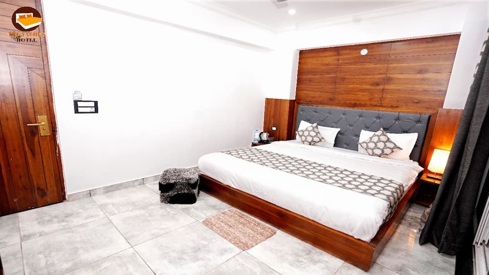 A cozy hotel room features a neatly made bed with patterned bedding, wooden accents, soft lighting, and tiled floors, ideal for travelers seeking comfort and relaxation.